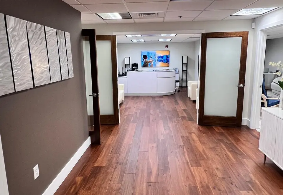 Wood-floored corridor through glass doors to the reception desk at Healthy Longevity Clinic Boca Raton